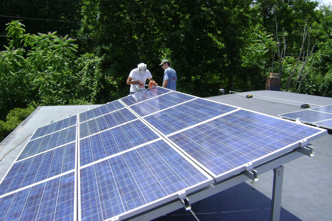 Deux techniciens fixent des panneaux solaires sur des châssis inclinés, sur un toit plat.